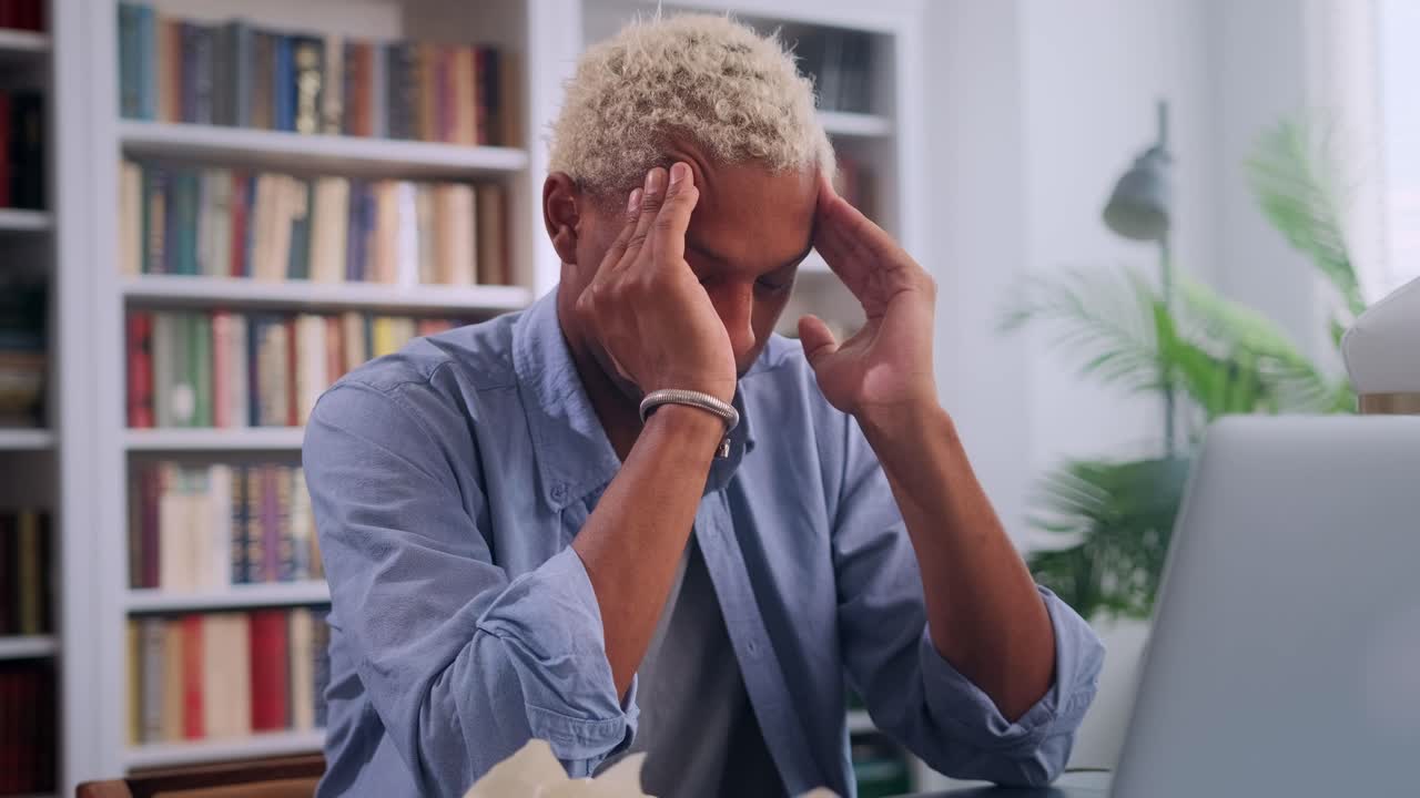 Young african american man doing massage temples sits with laptop in library