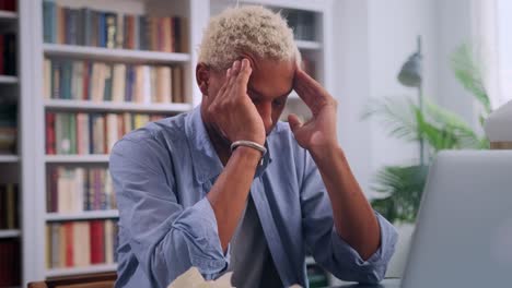 young african american man doing massage temples sits with laptop in library