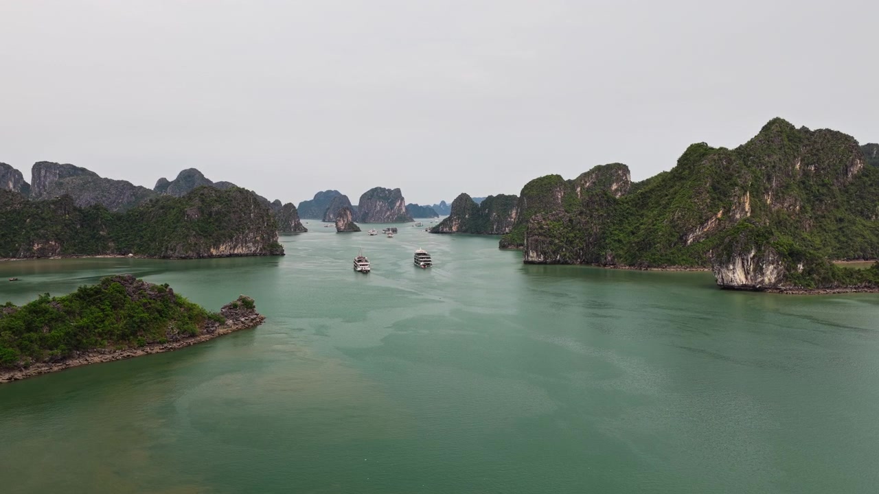 Cảnh quay rộng từ trên cao Vịnh Hạ Long Việt Nam với các du thuyền đang lướt trên mặt biển xanh ngọc bích tĩnh lặng, được bao quanh bởi các đảo đá vôi karst.