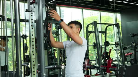 a man in a gym adjusts a cable machine, preparing for a workout. bright lighting and modern equipment create an energetic atmosphere