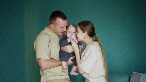 man holding a cute blond baby boy chewing a toy. mom takes a toy from a kid and plays teasing with child.