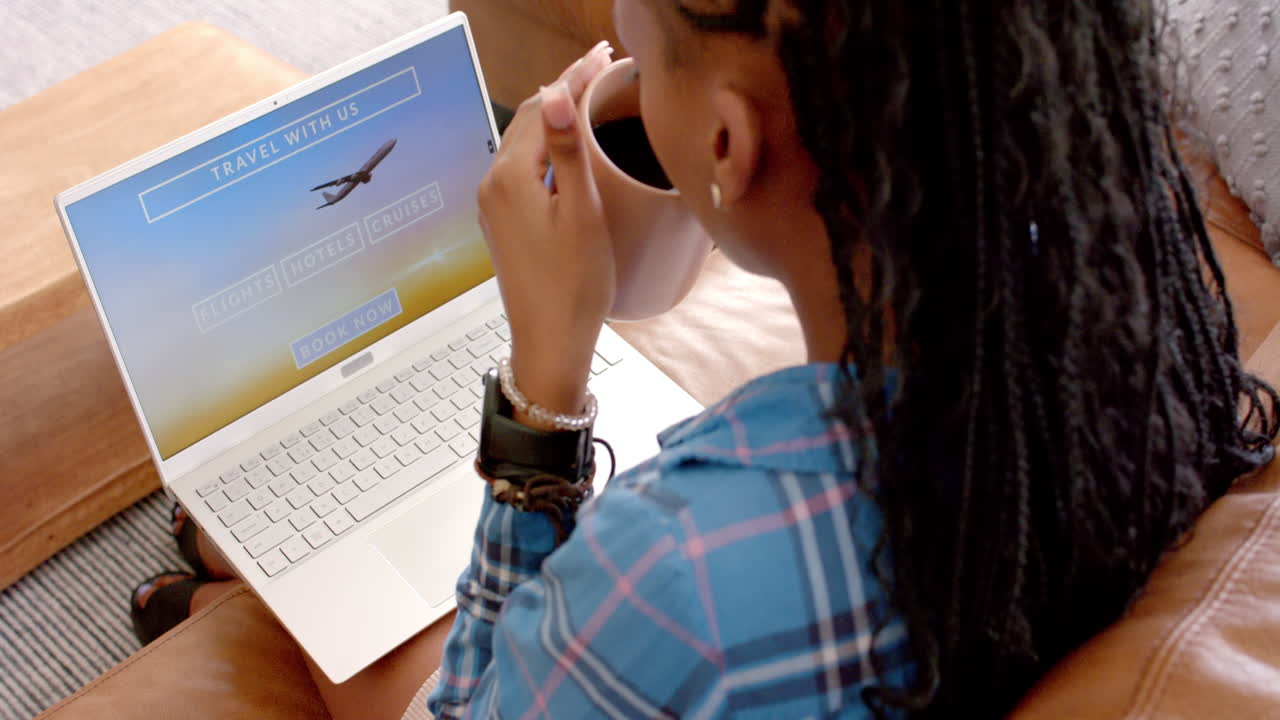 African American young woman booking travel online, sipping coffee
