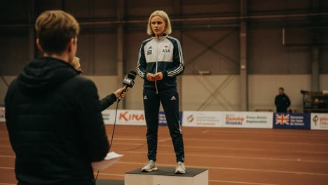 an athlete stands confidently on a podium during a press interview, showcasing sportsmanship and dedication while addressing a crowd of reporters in a vibrant indoor arena