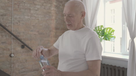 el anciano bebe agua y descansa después de hacer ejercicio y estirarse en casa