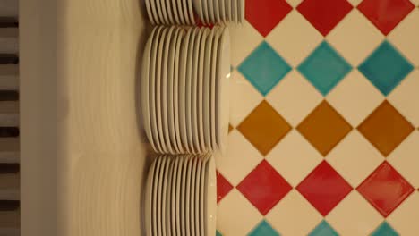stacks of clean white plates against a colorful tiled wall