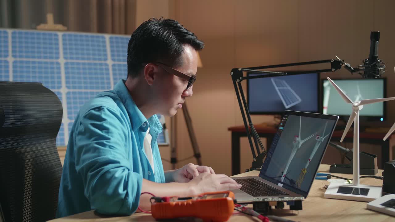 Side View Of Asian Man Looking At A Laptop Showing Wind Turbine On The Table That Next To The Solar Cell At The Office
