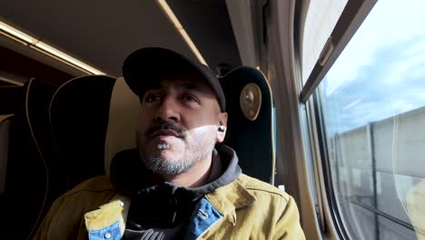 a man sitting on a train gazing outside the window with a pensive expression.