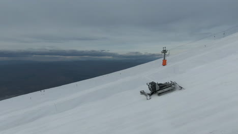 large snow groomer grooming snow on side of large mountain in the alps