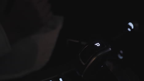 close up of modern car gear selector showing illuminated park mode letter p at night with soft light reflection and driver hand resting near control unit inside vehicle cabin