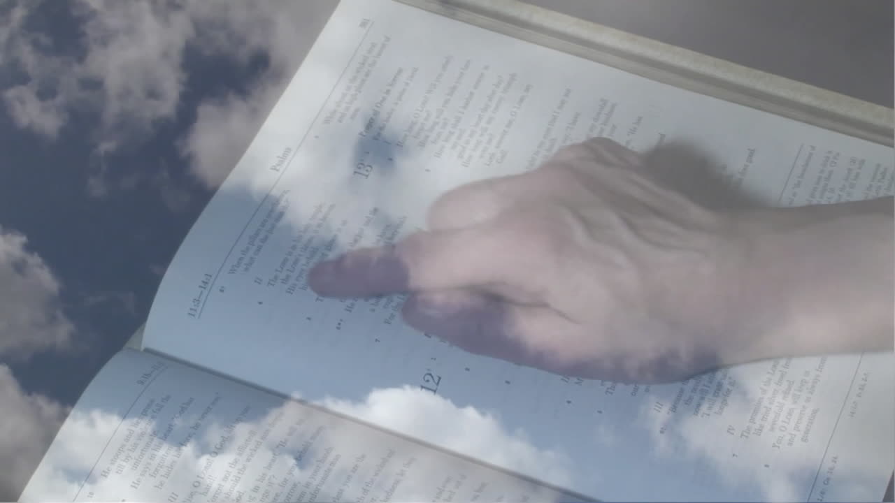 Animation of clouds over hand of caucasian man reading bible