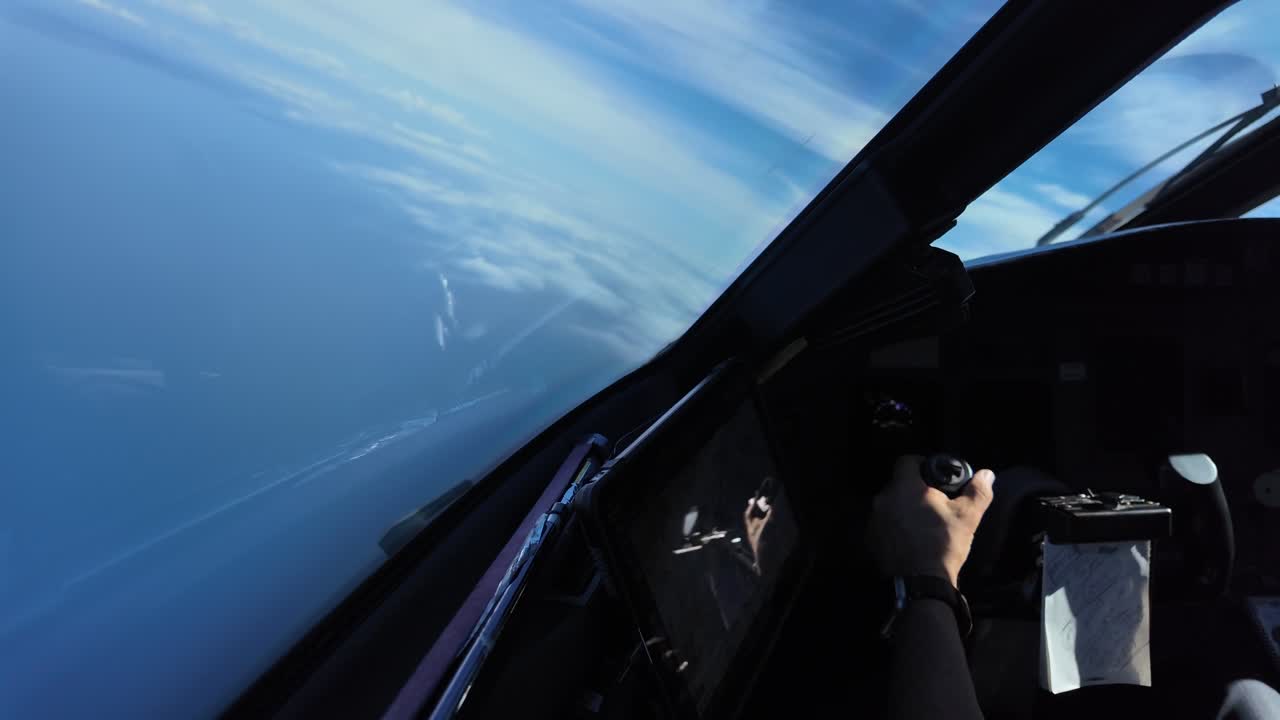 Mano di un pilota caucasico illuminata dalla luce del sole che afferra la cloche di un aereo a reazione mentre vola sopra il mare effettuando una virata a sinistra.