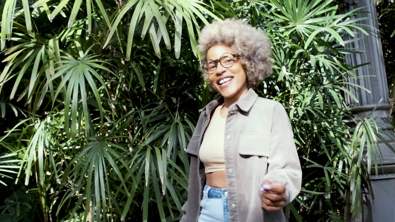 Una mujer con pelo rizado posando delante de unas plantas