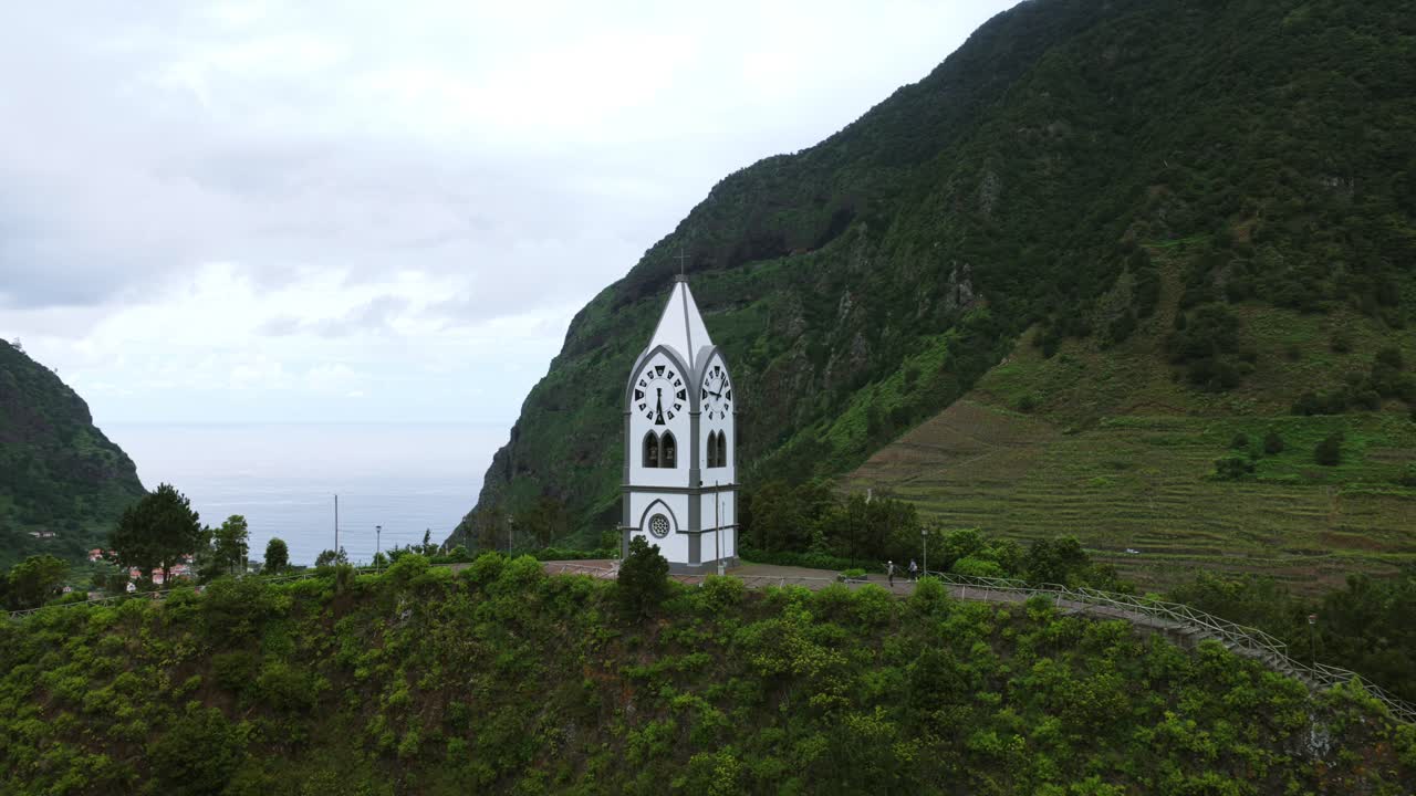 A white chapel overlooks lush greenery and hills, representing tranquility and heritage.