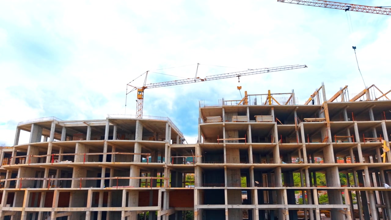 Low angle view of multi story concrete building under construction. Low angle shot of raw concrete framework of an apartment building with a tower crane under a cloudy sky.