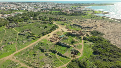 aerial view sprawling archaeological site of the tombs of the kings in paphos, cyprus, nestled between the cityscape and the coast, highlighting the ancient ruins amid modern urban development