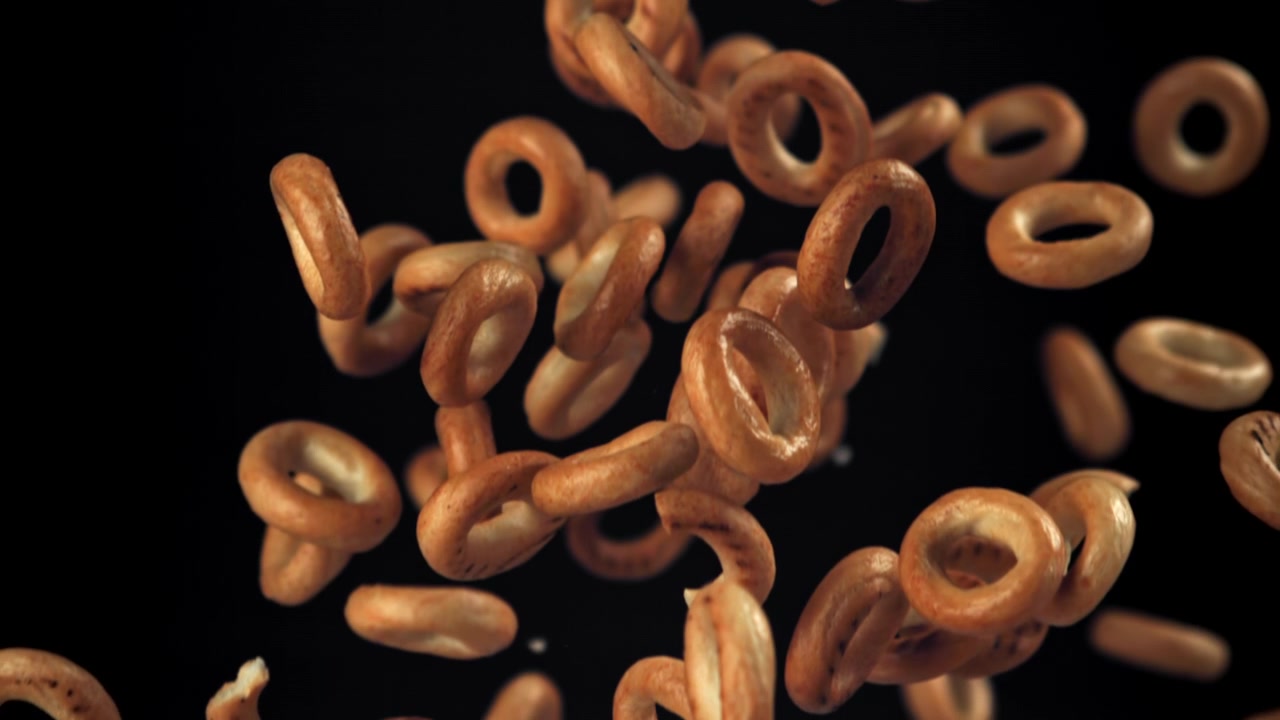 Golden Brown Bagels Falling in Slow Motion Against Black Background