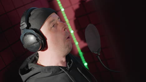 a man dressed in black, passionately singing into a microphone in a soundproofed recording room. his face shows intense expression and focus, fully immersed in the performance