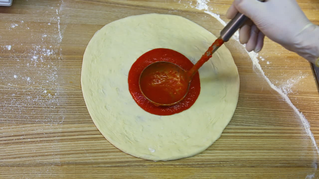 Chef spreading tomato sauce on pizza dough with ladle. Traditional pizza restaurant. Food video footage. Close-up.