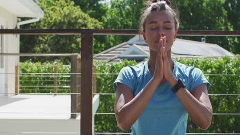 mujer biracial relajada sentada en la terraza y meditando