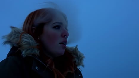 a young woman with red hair standing against a cold, blue winter background, exhaling visible breath in a chilly environment, capturing the essence of frosty conditions