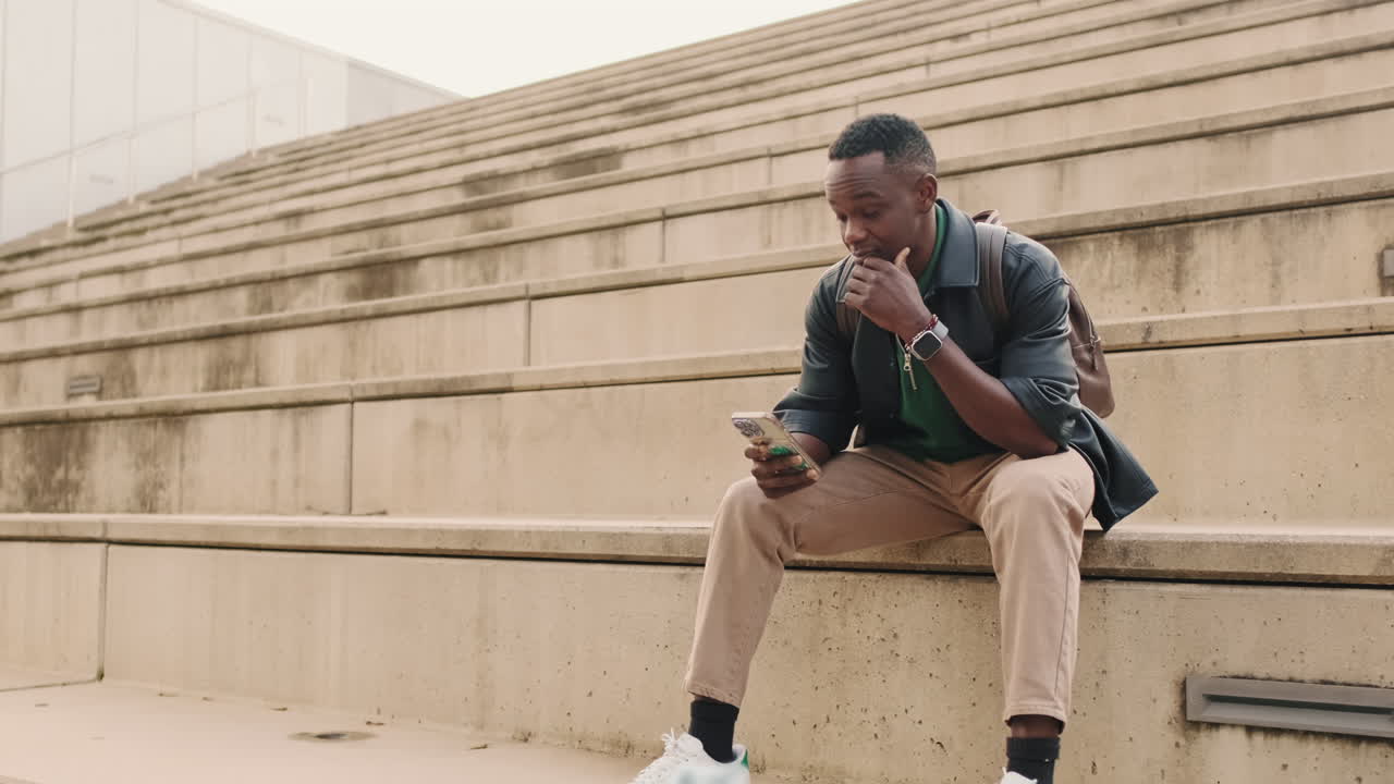 Young Man Sitting on Steps and Using Smartphone