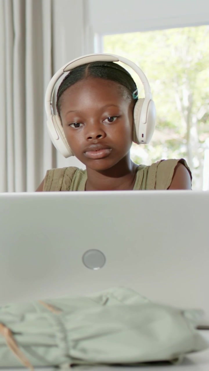 Vertical video: Focusing student starting study on laptop at home wearing green top and headphones