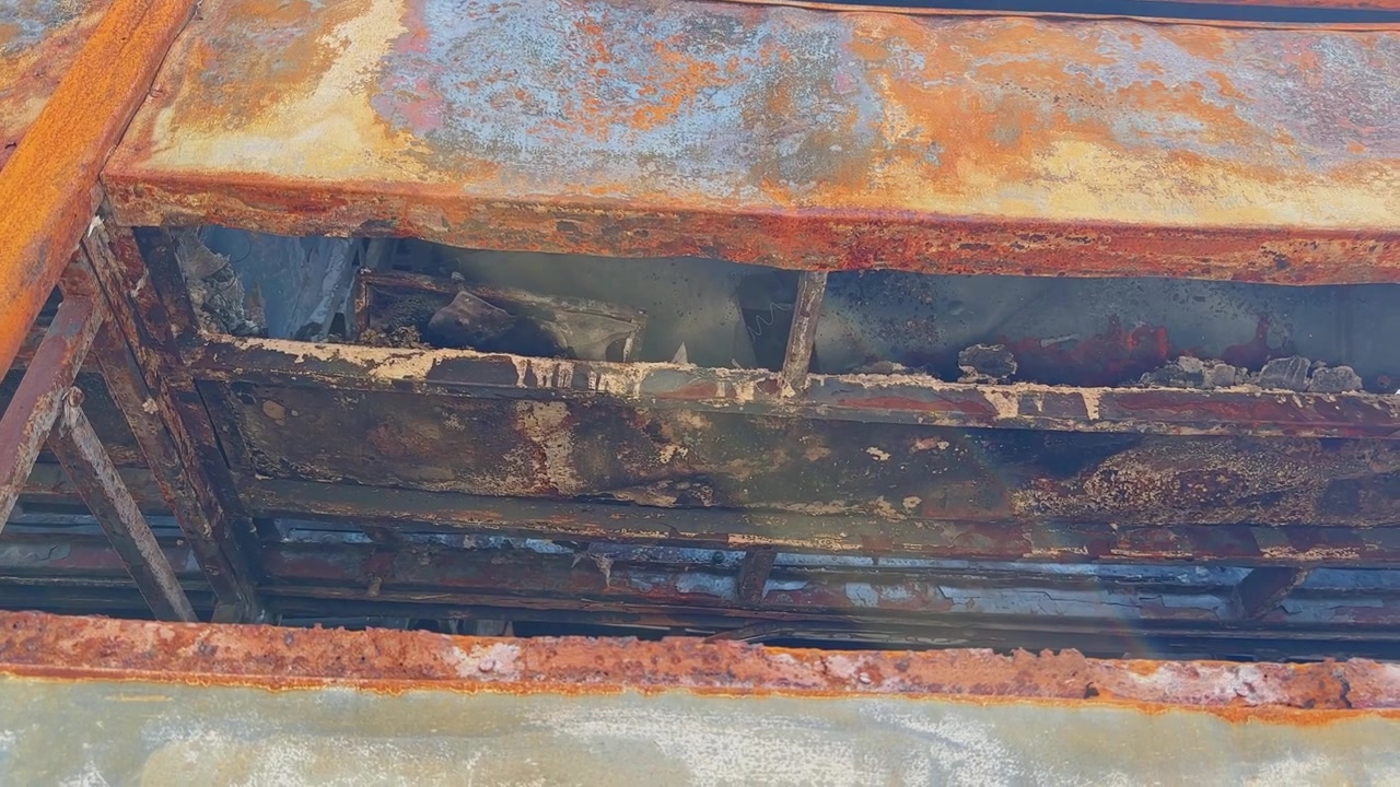 Съемка с проводкой снаружи поврежденного огнем спального автобуса, показывающая ржавую оконную раму, обугленный металлический корпус и разрушенный интерьер через проем!