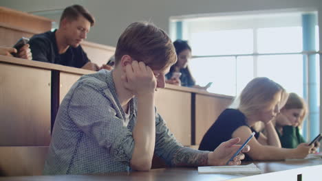 a group of men and women in a large university audience silently look at the screens of smartphones and write chat messages. each person looks at the screens of his device without paying attention to the events of the real world.