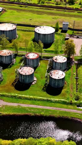 aerial of decaying wastewater tanks beside river and overgrown industrial area, vertical aerial establishing