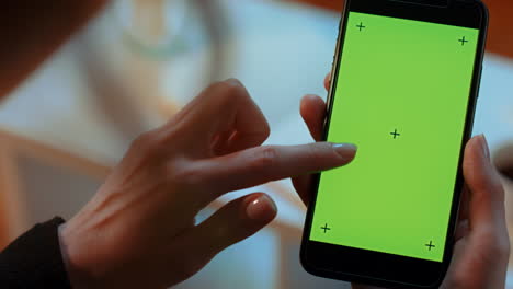 pan lento de una mujer caucásica sosteniendo un teléfono celular de pantalla verde con marcas de seguimiento mientras se desplaza hacia abajo con el dedo dos veces
