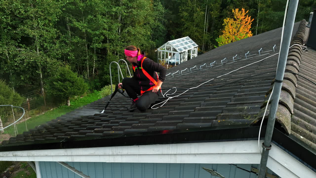 Aerial view of a woman pressure washing house roof tiles, sunny, autumn day