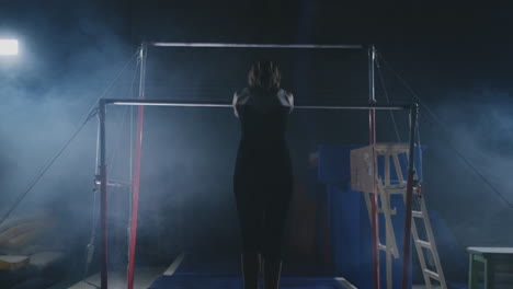 competitions in gymnastics. a woman walks to the crossbar and performs dips flip-flops in slow motion on a dark background in backlight. slow motion.