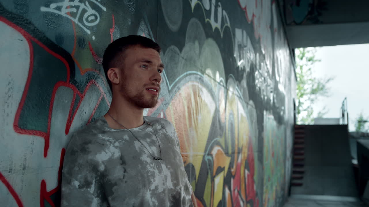 그래피티와 함께 벽 근처에서 휴식을 취하는 젊은  ⁇ 스터. 조용한 밀레니얼은 멀리보고.