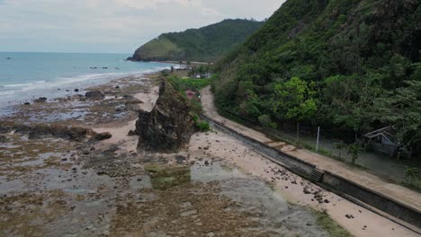 a stunning wide drone shot reveals a verdant mountain beside the shoreline, with a scenic coastal road weaving through the landscape.