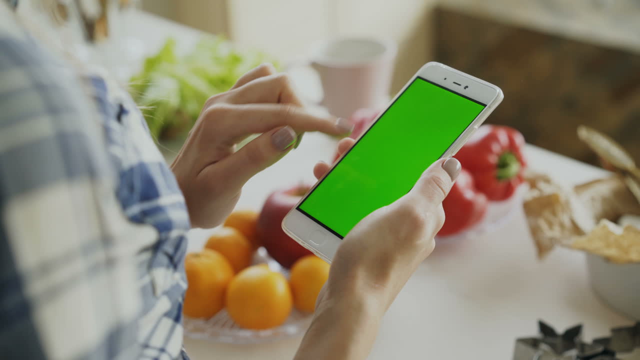 Woman using smartphone in kitchen with food in background