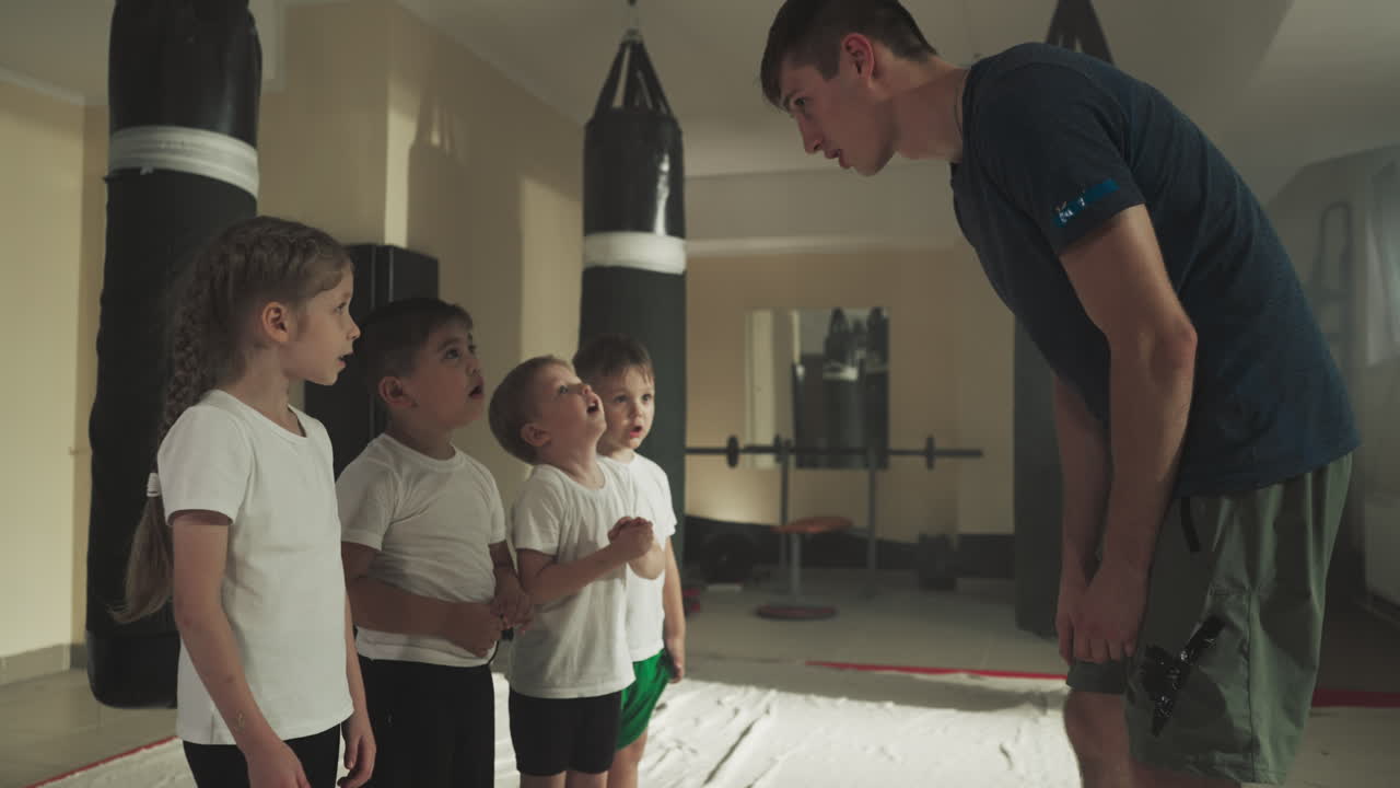 아이들은 체육관에서 블록을 보여주는 트레이너를보고 재미있는 초등 학생들은 스포츠 클럽의 스로우 모션에서 강사로부터 전투 기법을 배니다.