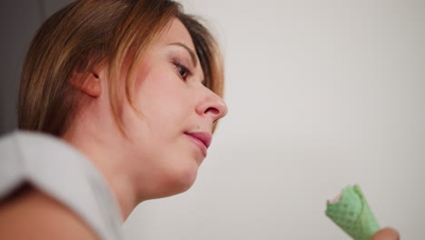 close up side view of white woman savoring chocolate ice cream cone with relaxed expression, enjoying sweet dessert in casual indoor setting