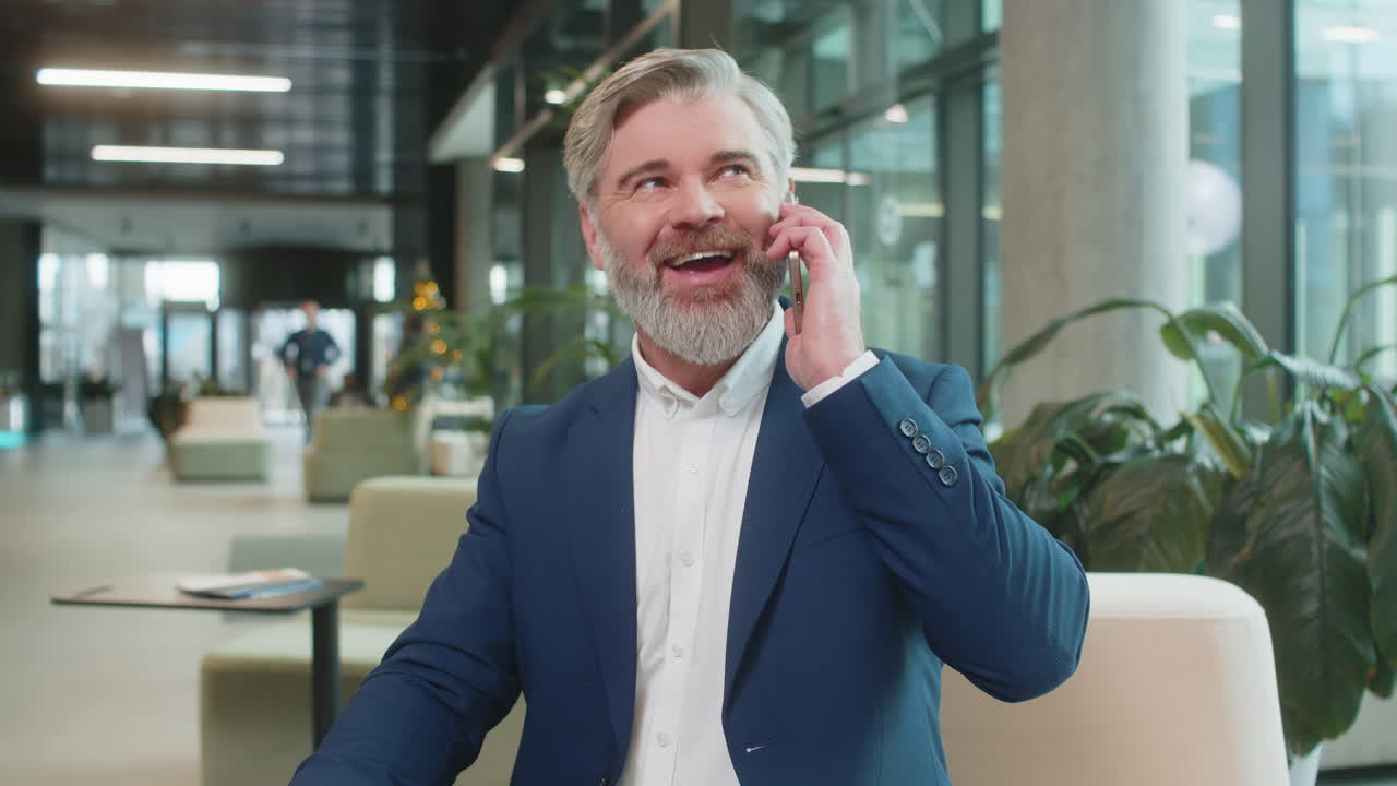 Moden forretningsmand i formelt jakkesæt besvarer klienten på mobiltelefonopkald i moderne kontorlobby