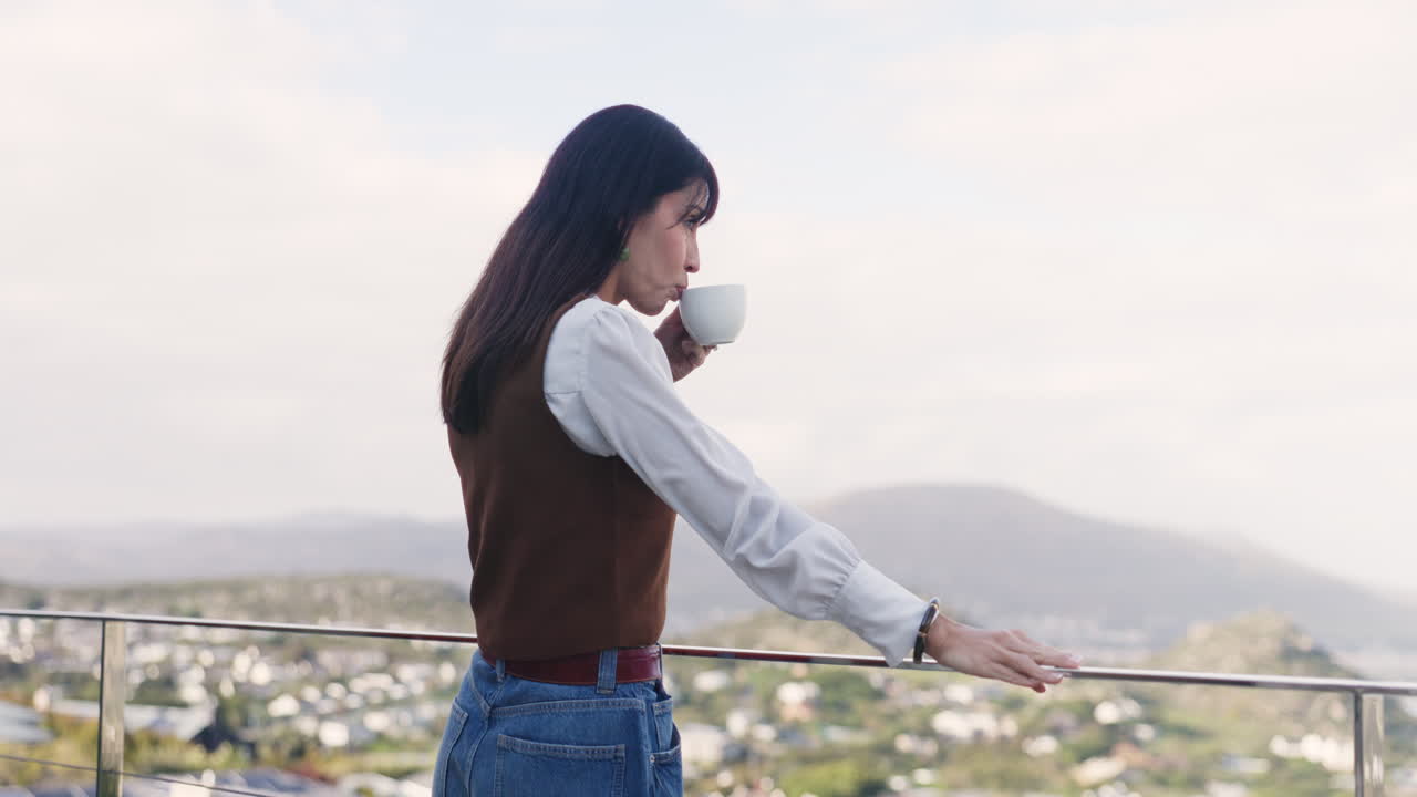 Người phụ nữ thưởng thức cà phê trên ban công với khung cảnh đô thị tuyệt đẹp