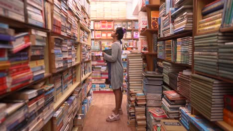 asian girl standing between the rows of bookshelves and exploring, side angle shot