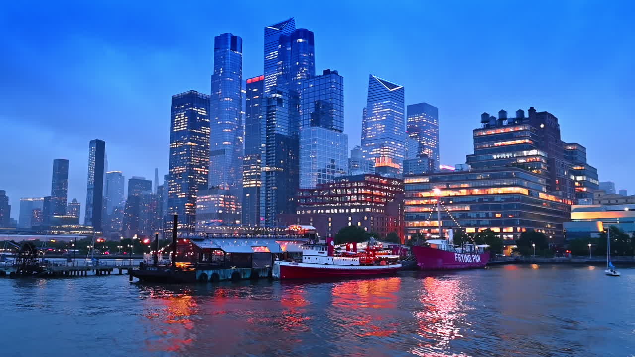 Beautifully lit boats, pier and buildings at the waterfront. Travelling by the Hudson River in New York at dusk time