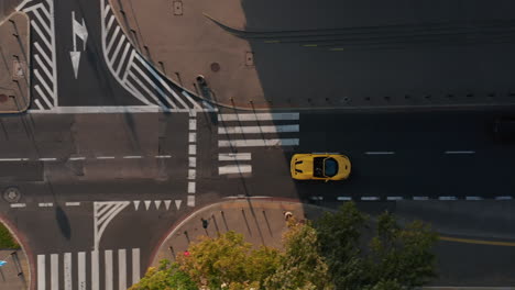 Aerial-birds-eye-overhead-top-down-view-of-yellow-convertible-car-turning-on-main-road.-Late-afternoon-sunlight-with-long-shadows.-Warsaw,-Poland