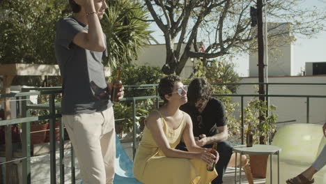 group of happy friends holding beer and relaxing while having a rooftop party on a summer day