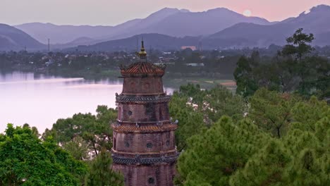 This-footage-captures-a-peaceful-sunset-over-Hue,-Vietnam,-featuring-a-beautiful-pagoda-surrounded-by-lush-trees,-with-the-city-and-distant-mountains-in-the-background