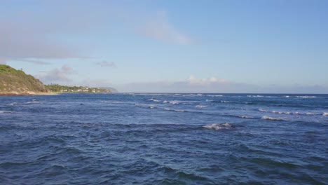 drone footage across the white capped blue pacific ocean waves on a sunny day on oahu hawaii with blue skies and the coast of the hawaiian island on the left