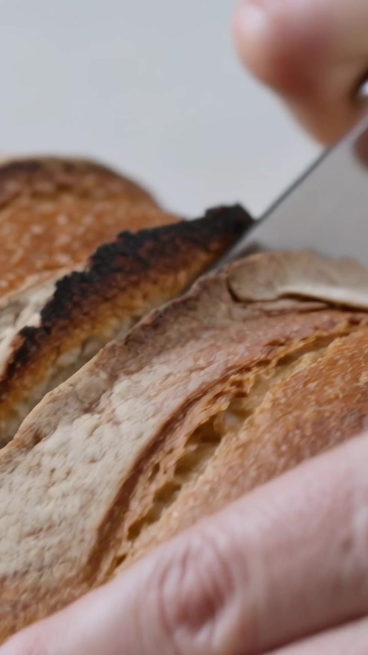 Vertical video: Slicing crusty loaf hands holding and moving bread knife to show crumb in kitchen