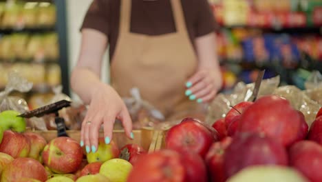 Close-up-of-a-girl-supermarket-worker-in-a-brown-T-shirt-and-apron-arranging-apples-on-the-counter-during-her-work-shift-at-the-supermarket