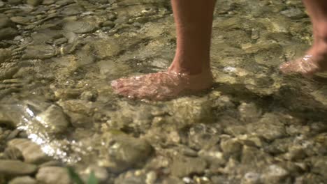 man walking barefoot in pure cold clear river, slow motion closeup