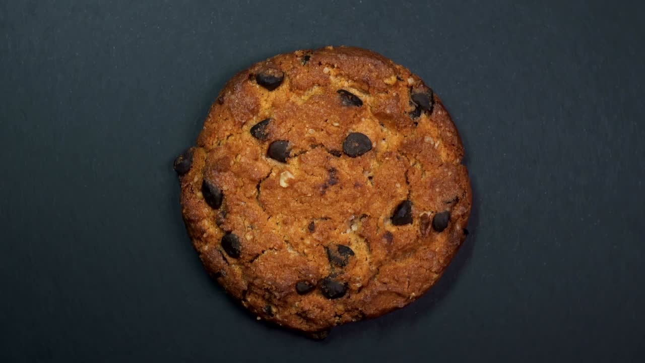 Chocolate chip cookie close-up, macro shot, slowly spinning on a rotating black background.