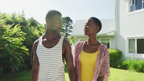 happy african american couple walking holding hands in sunny garden smiling